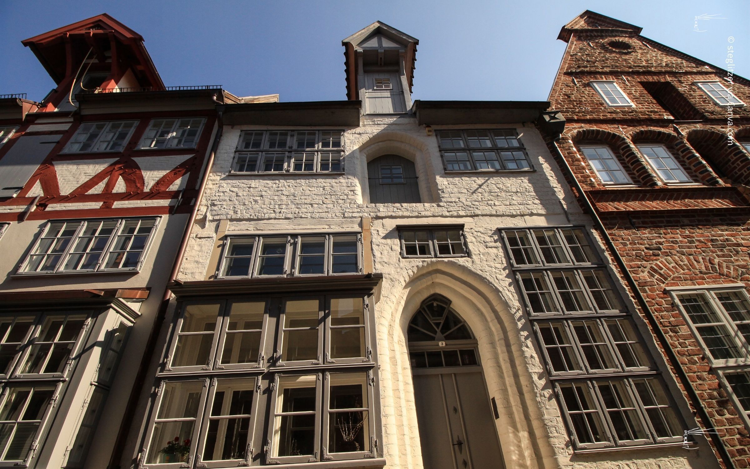 Die Fassade traditioneller europäischer Gebäude mit unterschiedlichen Architekturstilen und Fensterdesigns, aus einem niedrigen Winkel vor einem klaren blauen Himmel betrachtet, spiegelt Leichtigkeit wider.